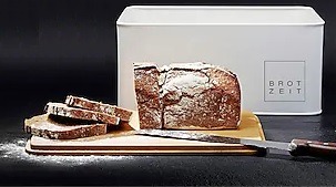 Brot auf Schneidebrett mit Brotmesser vor Brotkasten