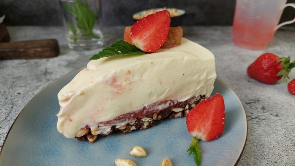 no-bake Rhabarber Cheesecake, mit schokoladen Knusperboden, Stück auf Teller, Erdbeeren, Rhabarber-Fruchteinlage